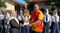 Guru PJOK SMP Negeri 1 Kalimanah, Dedi Irwanto menerima piala kejuaraan dari Plt Kepala SMP Negeri 1 Kalimanah, Tjandra Irawati usai upacara bendera di sekolahan itu, Senin 18 Mei 2026